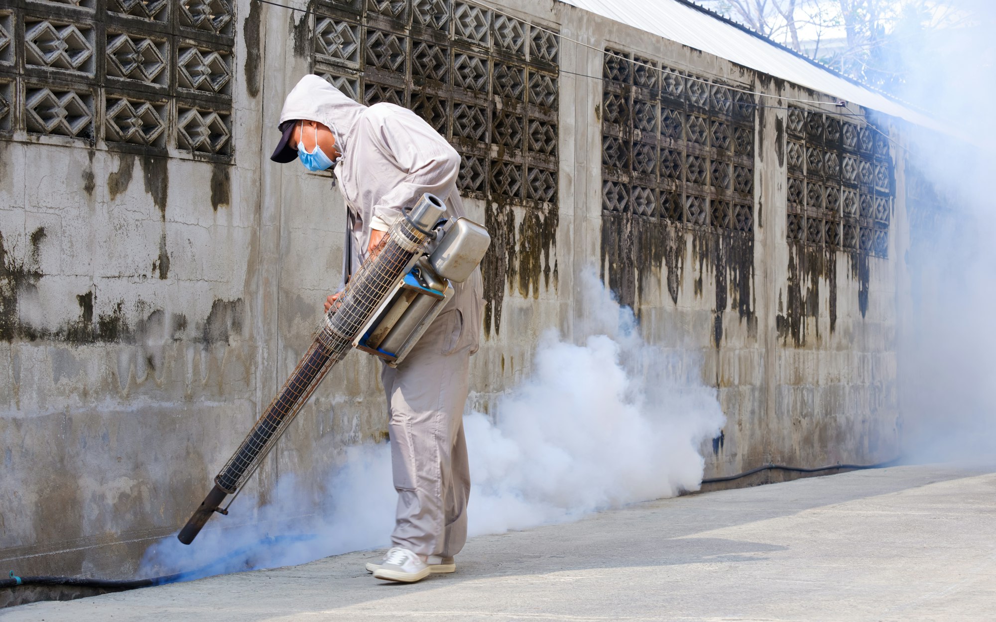 Healthcare worker using fogging machine to fumigation for eliminate mosquitoes in drainage ditch